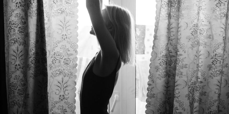 A person stretching in silhouette against a large window.